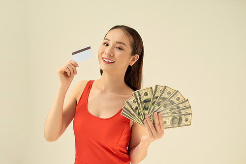 Happy young woman with cash money and credit card on gray background