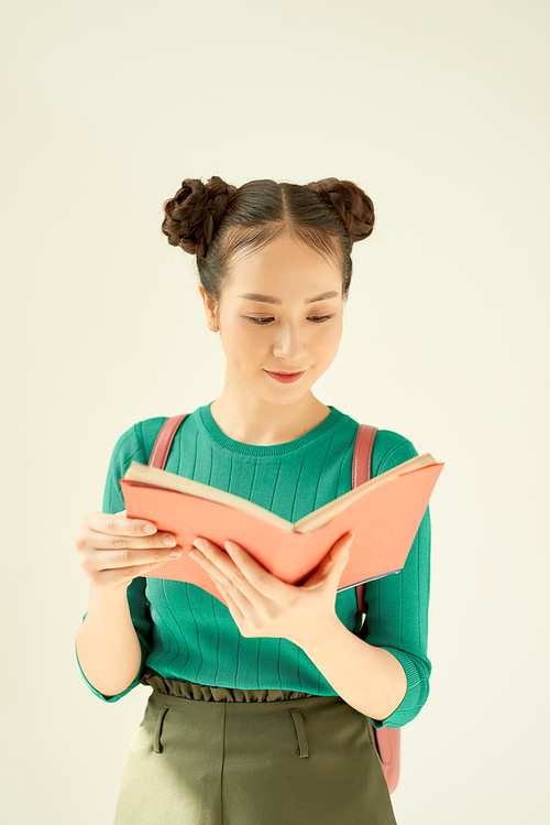 Portrait of a smiling female teenager with backpack  reading book isolated on a white background