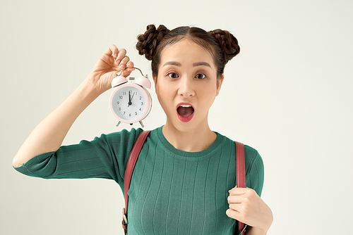 Image of screaming young confused woman standing isolated over white background. Looking aside holding alarm clock.