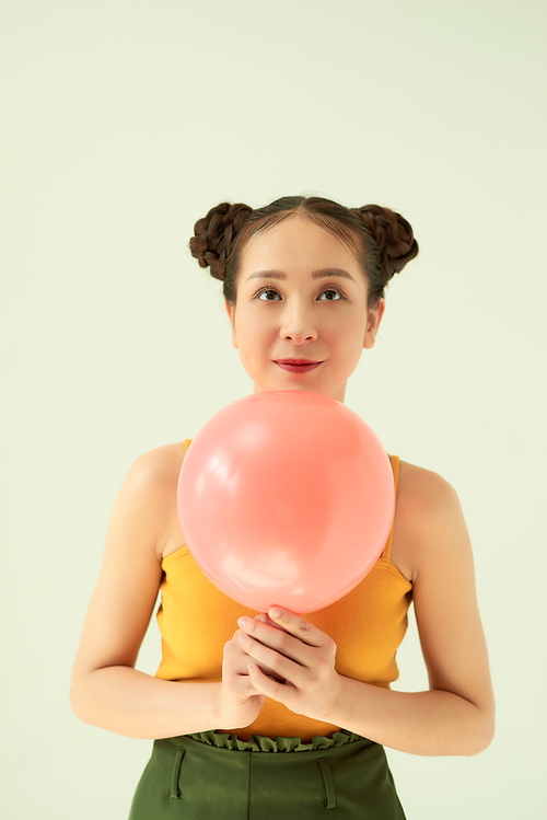 Lovely cheerful Asian teenager girl holding pink air balloon with two buns hairstyle over light background.