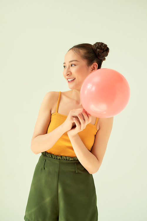 Lovely cheerful Asian teenager girl holding pink air balloon with two buns hairstyle over light background.