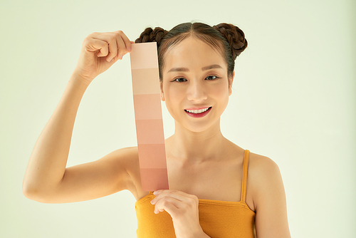 Young Asian woman showing skin tone palette while standing isolated on light background.