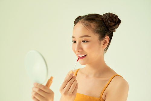Beautiful young Asian woman applying lipstick over light background.