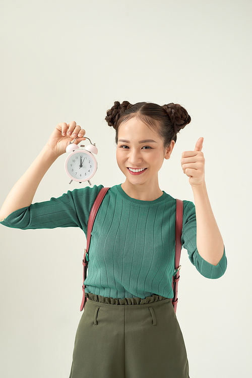 Young woman holding classic alarm clock over light background happy with big smile doing ok sign, thumb up with fingers, excellent sign