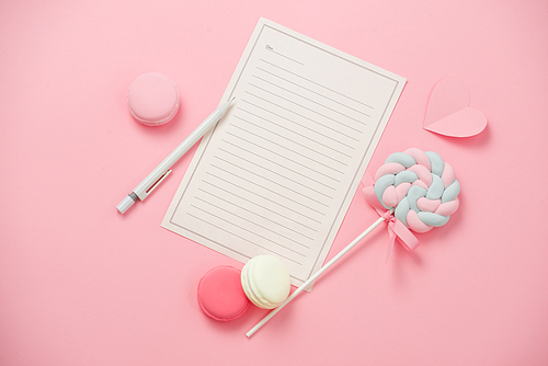 A white sheet of paper for message to loved one, macaron, candy on pink background. Happy womans day concept. Mock up