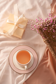 Cup of tea, gift box and flowers on light background