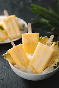 Overhead view of yellow ice lollies inverted in a white bowl on dark table