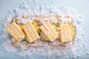 Yellow fruit popsicles on a plate. Top view over a blue wood background.