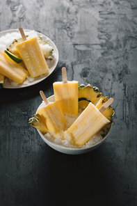 Overhead view of yellow ice lollies inverted in a white bowl on dark table