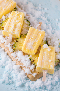 Yellow fruit popsicles on a plate. Top view over a blue wood background.