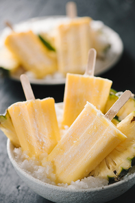 Overhead view of yellow ice lollies inverted in a white bowl on dark table