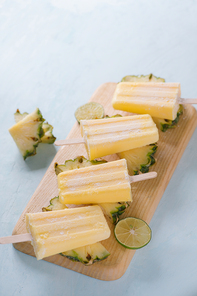 Pineapple popsicles on a marble paddle board. Top view over a blue wood background.