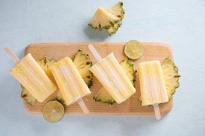 Pineapple popsicles on a marble paddle board. Top view over a blue wood background.