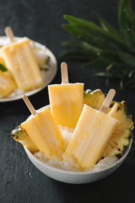 Overhead view of yellow ice lollies inverted in a white bowl on dark table