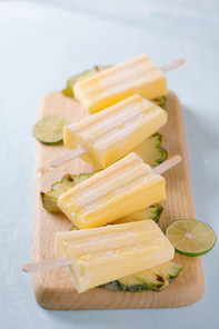 Pineapple popsicles on a marble paddle board. Top view over a blue wood background.