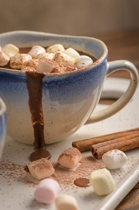 Cup of hot chocolate drink with marshmallows and cinnamon on brown wooden background.