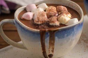 Cup of hot chocolate drink with marshmallows and cinnamon on brown wooden background.