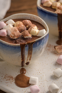 Cups of hot chocolate drink with marshmallows and cinnamon on brown wooden background.