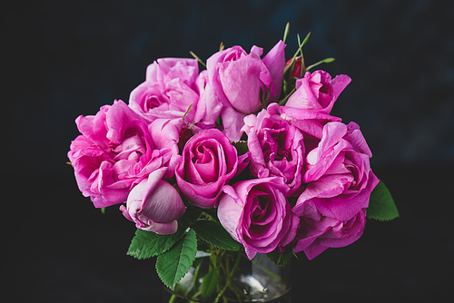 Bouquet of small pink garden roses in vase on dark background