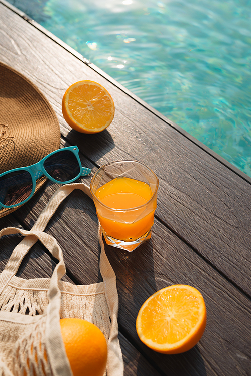 Beach hat, orange juice and sunglasses near the swimming pool