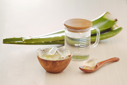 Bowl with peeled aloe vera, green leaves and aloe bottle glass on wooden background