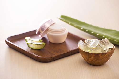 Aloe vera cosmetic cream on wooden tray with aloe leave and bowl on light background.