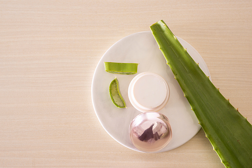 Jar of cream with alo leave and chopped aloe on marble round board