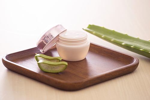 Aloe vera cosmetic cream on wooden tray with aloe leave on light background.