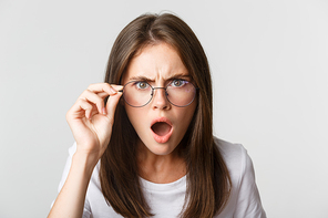 Close-up of insulted and shocked young angry woman looking from under glasses.