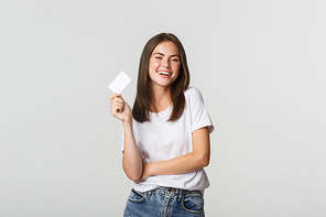 Attractive happy brunette girl laughing and holding credit card, white background.