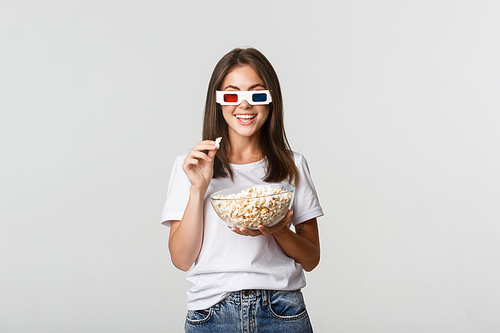 Amused pretty young woman in 3d glasses watching movies or tv series, eating popcorn and smiling thrilled.