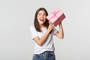 Intrigued happy birthday girl shaking gift box to find out what inside.