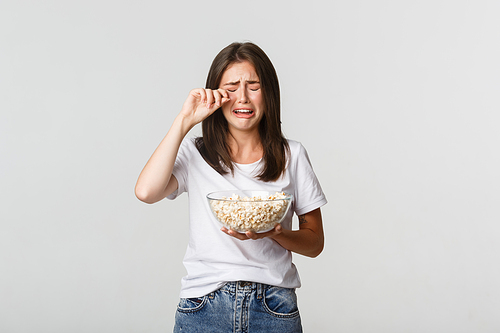 Portrait of crying young cute girl watching drama movie or tv series with bowl of popcorn.
