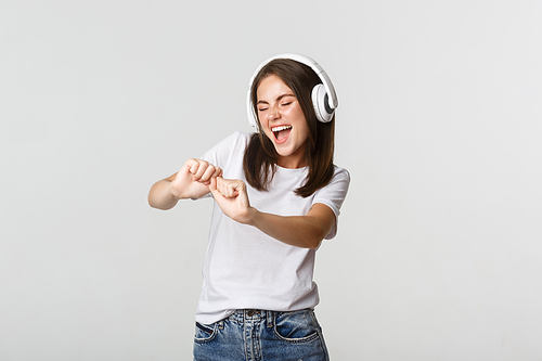 Joyful beautiful young woman dancing, enjoying music in wireless headphones.