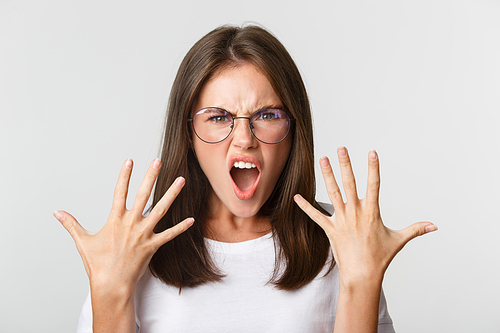 Close-up of angry and furious young woman in glasses arguing, complaining over white background.