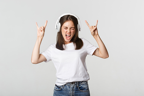Joyful beautiful girl in headphones dancing, showing rock-n-roll signs.