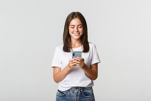 Smiling attractive girl using mobile phone and looking at screen pleased.