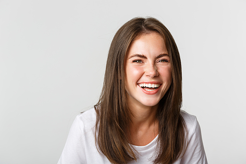Close-up of happy and carefree brunette girl smiling and laughing from joy, standing white background.