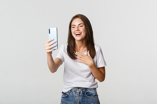 Friendly smiling woman video calling and talking on smartphone happy, standing white background.