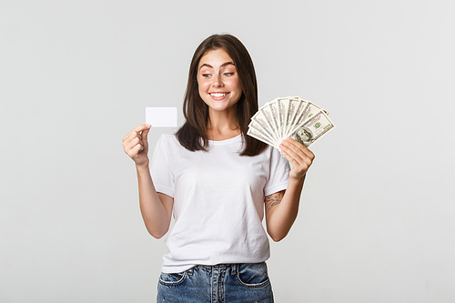Portrait of excited smiling girl holding money and credit card, white background.