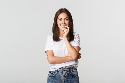 Smiling attractive girl biting finger and looking with temptation, white background.