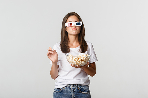 Skeptical beautiful woman in 3d glasses, holding popcorn and looking perplexed, thinking while watching movie.