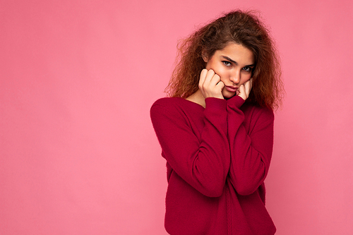Portrait of young emotional offended touchy cute brunette curly woman with sincere emotions wearing trendy pink pullover isolated on pink background with copy space and taking offence.