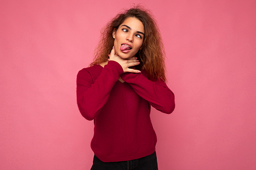 Portrait of young emotional beautiful brunette curly woman with sincere emotions wearing trendy pink pullover isolated on pink background with copy space and keeping hands on neck and strangling herself.