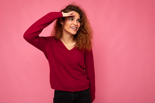 Portrait of young positive happy joyful beautiful brunette curly woman with sincere emotions wearing trendy pink pullover isolated on pink background with copy space and looking to the side.
