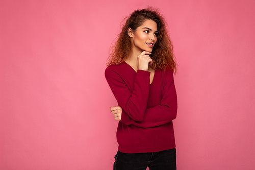 Photo of young european thoughtful fascinating brunette curly woman with sincere emotions wearing trendy pink sweater isolated over pink background with free space.