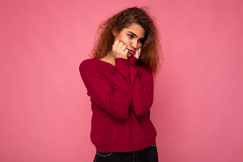 Portrait of young emotional offended touchy beautiful brunette curly woman with sincere emotions wearing trendy pink sweater isolated on pink background with copy space and taking offence.