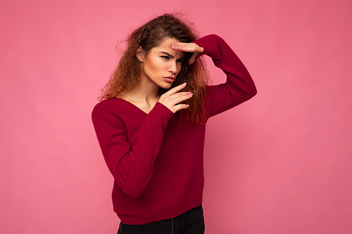 Portrait of young serious beautiful brunette curly woman with sincere emotions wearing trendy pink pullover isolated on pink background with copy space and grimacing having fun.