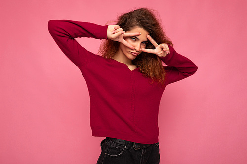 Portrait of young positive happy joyful beautiful brunette curly woman with sincere emotions wearing trendy pink pullover isolated on pink background with copy space.