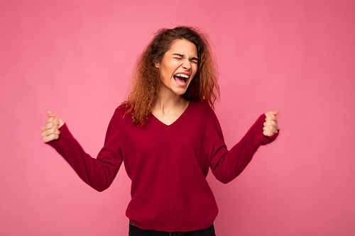 Photo of young emotional happy positive delightful beautiful brunette curly woman with sincere emotions wearing casual pink pullover isolated over pink background with copy space.
